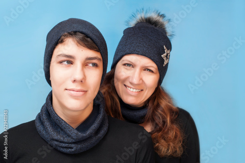 A boy with his mother wearing a blue background wearing warm winter hats and scarves smiling