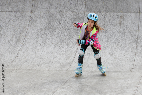 Little girl riding on roller skates in a helmet and knee pads