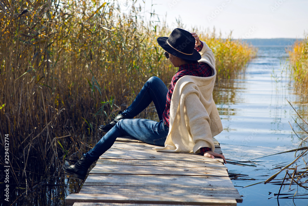 woman in a black hat and sweater sits on the old pier to the bushe