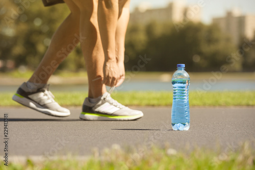 Health drinking water concept. Male runner tying his shoe next to bottle of water.
