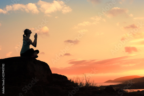 Beautiful silhouette of young female praying on a mountain top. 