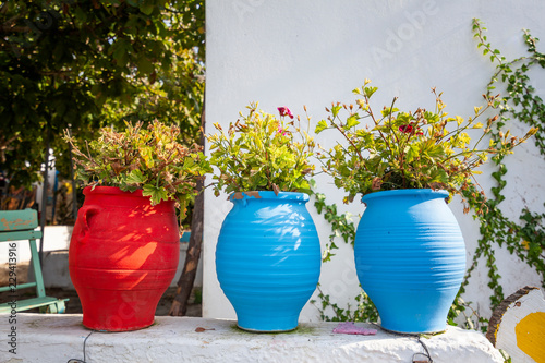 Fototapeta Naklejka Na Ścianę i Meble -  Bright blue and red ceramic pots with flowers on the street, against the white walls, street decoration, island of Kos, Greece