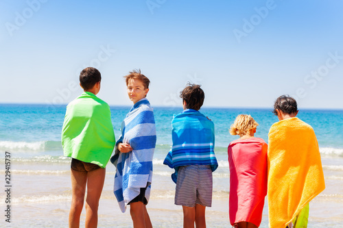 Boys wrapped in beach towels looking at sea