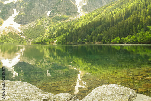 A beautiful view of the 'Morskie Oko' lake in the Polish Mountains in the Tatras. Green trees are reflected from the water's surface. A beautiful landscape from the perspective of a tourist.
