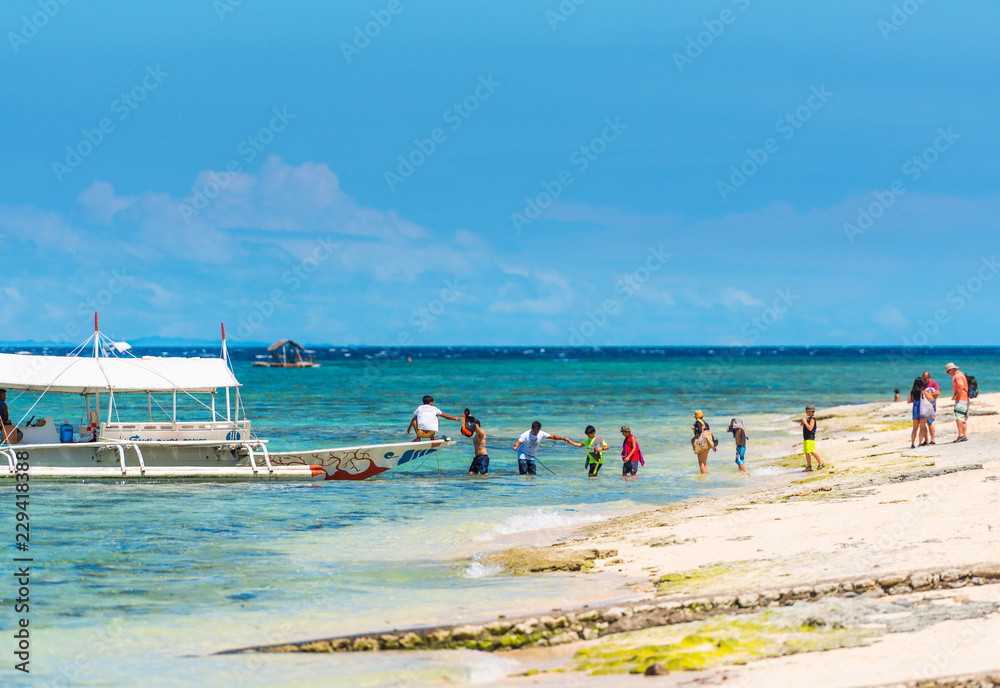 MOALBOAL, PHILIPPINES - FEBRUARY 20, 2018: Boat and a group of tourists near the shore. Copy space for text. MOALBOAL, PHILIPPINES - FEBRUARY 20, 2018: Boat and a group of tourists near the shore. Copy space for text.