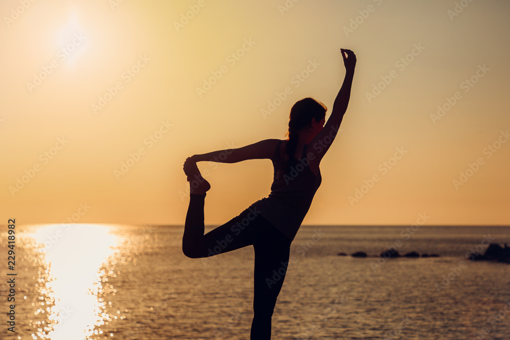 Women silhouette at the sunset. Practicing yoga on the beach