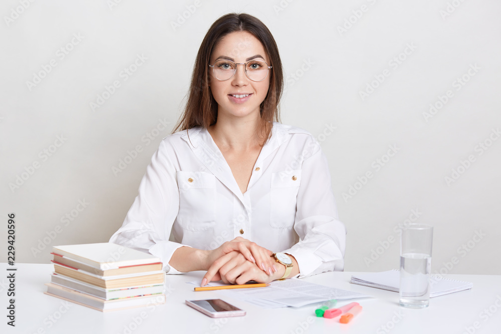 Satisffied female archiect learns design, spends time with preparation for course wowk, uses scientific literature, fills in documents, wears round spectacles, isolated over white background. Satisffied female archiect learns design, spends time with preparation for course wowk, uses scientific literature, fills in documents, wears round spectacles, isolated over white background.
