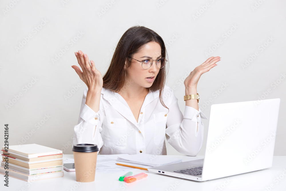 Puzzled emotive woman has deadline task, gesture with frustration, stares with bugged eyes, wears round spectacles for good vision, drinks coffee, isolated over white background. So what to do? Puzzled emotive woman has deadline task, gesture with frustration, stares with bugged eyes, wears round spectacles for good vision, drinks coffee, isolated over white background. So what to do?