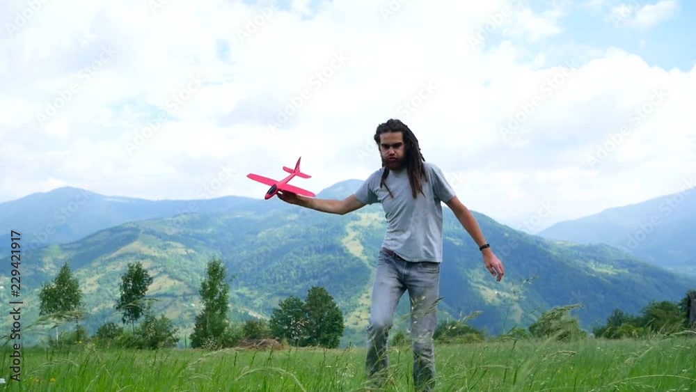 A young man with dreadlocks playing with a model airplane in the mountains A young man with dreadlocks playing with a model airplane in the mountains