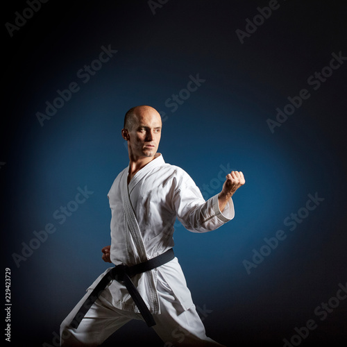 Athlete trains formal karate exercises on blue background with gradient