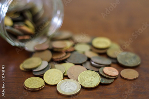 Coins spilling from a glass jar on a wooden table