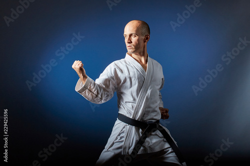 On a blue background with a gradient, an athlete with a black belt performs formal karate exercises.