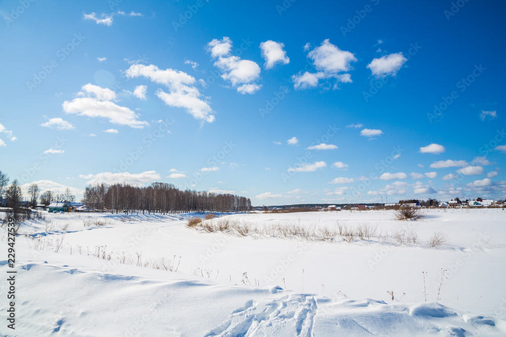 Winter landscape. Countryside. Frozen river. Sunny day. Blue sky. White clouds.