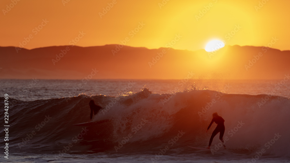 Silhouette of surfers riding a wave at sunrise in Jeffreys Bay