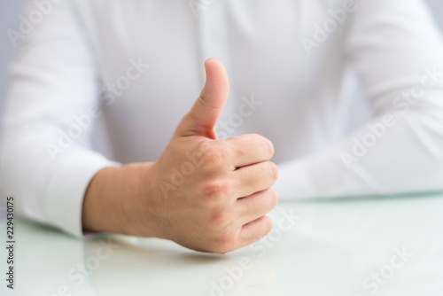 Close-up of unrecognizable businessman showing thumb-up. Man sitting at table and expressing approval. Gesture concept