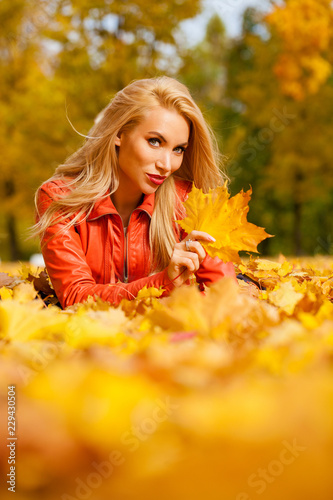 Beautiful blond hair woman lies down on leaves at the park on beautiful autumn