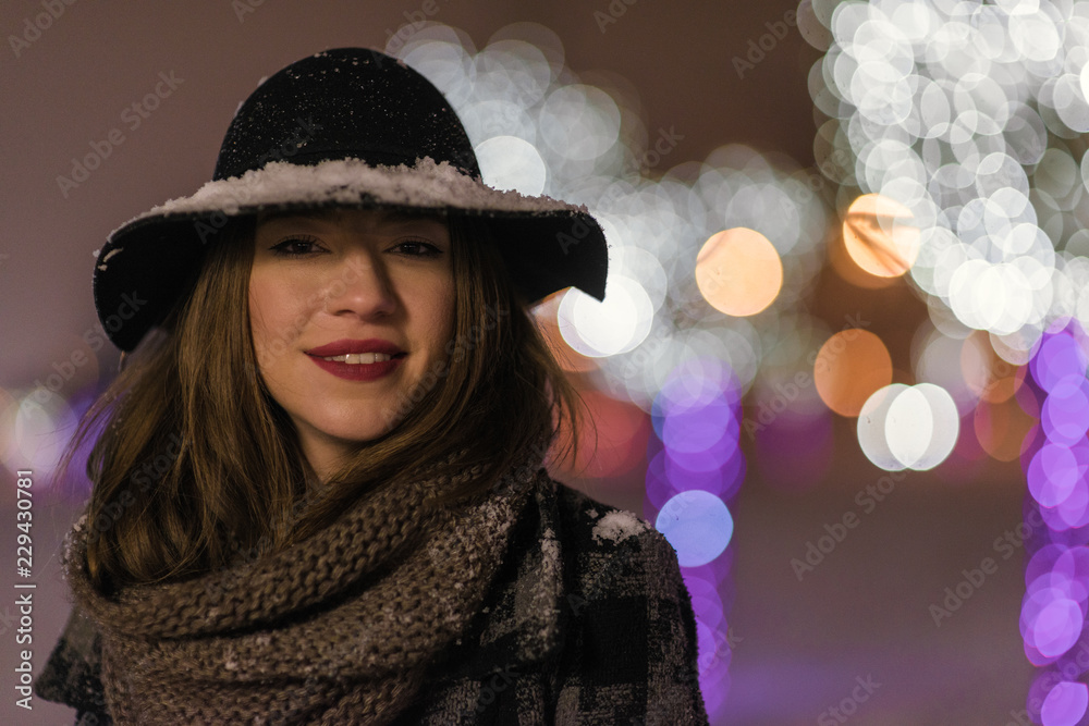 Young girl walking in front of trees decorated with colorful lights for christmas night, blurred in the background Young girl walking in front of trees decorated with colorful lights for christmas night, blurred in the background