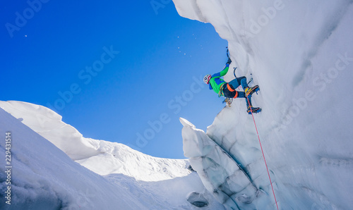 Epic shot of an ice climber climbing on a wall of ice. Mountaineer, climber or alpinist on an adventure extreme ascent with ice axe and crampons. Alpine extreme climbing on a serac or creavasse.