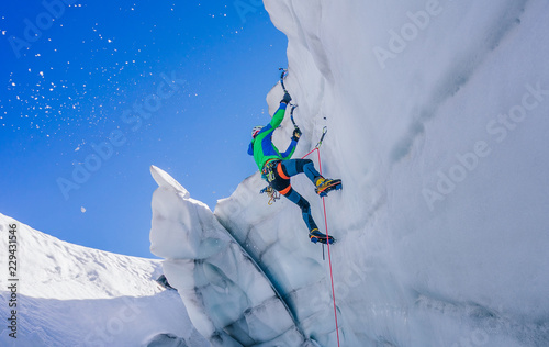 Epic shot of an ice climber climbing on a wall of ice. Mountaineer and climber on an adventure extreme ascent with ice axe and crampons. Alpine extreme climbing on a serac or creavasse. photo