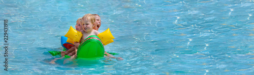 Drei Kleinkinder mit Riesenspaß auf einem Schwimmkrokodil im Schwimmbad photo