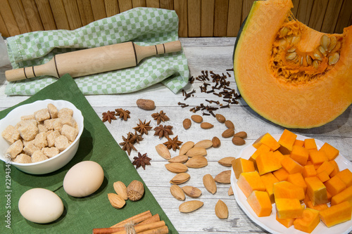 Fresh pumpkin and ingredient for bakery, eggs, cinnamon sticks and anise stars, a lot of almonds, brown cane sugar and nutmeg. Rolling pin and cookie cutter on wooden table background.