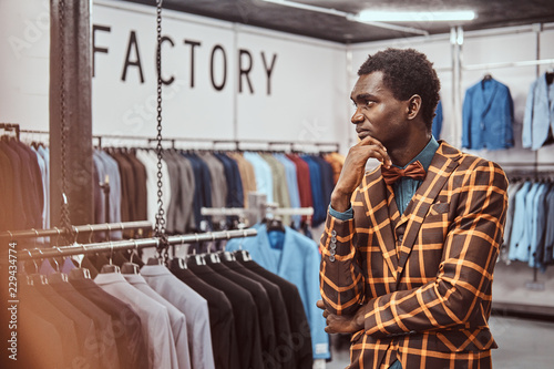 Fotografija Elegantly dressed African man posing with hand on chin while standing in a classic menswear store