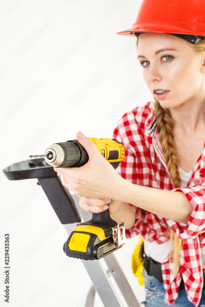 Woman using drill on ladder Woman using drill on ladder