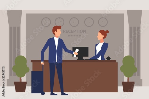 Young man giving reservation to woman receptionist that stands at reception desk.