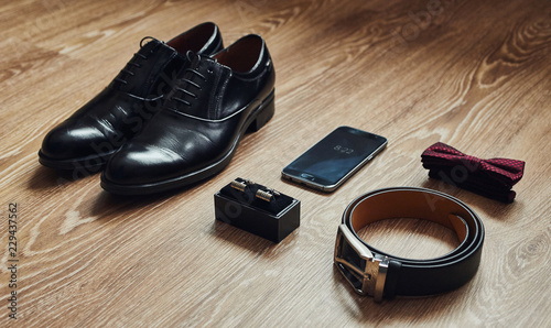 Different men's accessories such as: shoes, belt, bow tie, cufflinks and telephone - are on the table