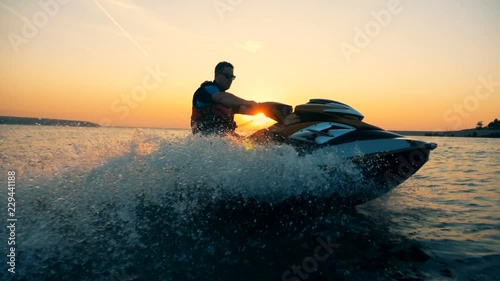 A man is riding a jet-ski along the coastline during sunset photo