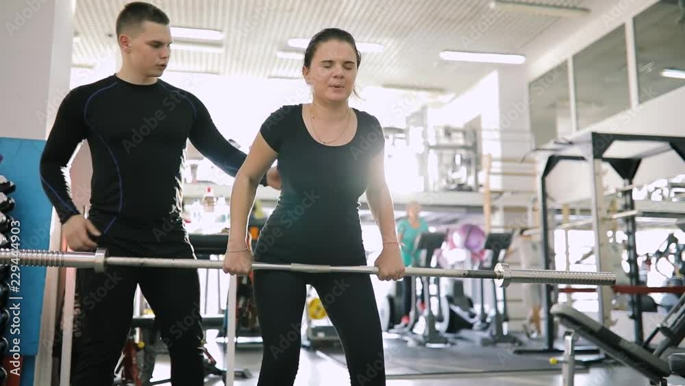 Personal fitness trainer helping make exercice with barbell for beginner woman in gym