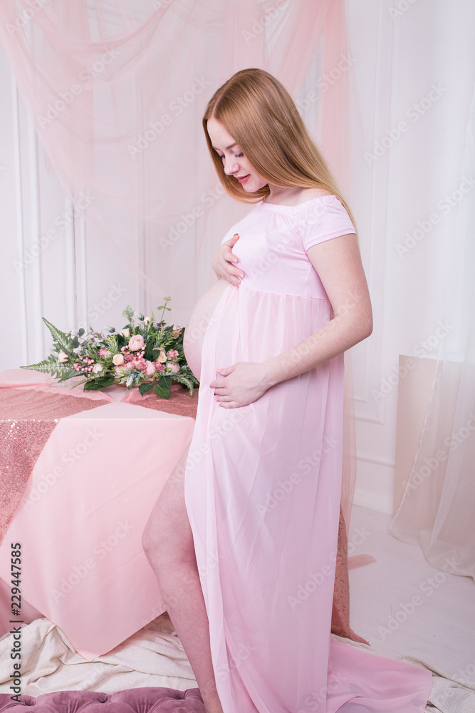 Happy pregnant woman in pink dress with flowers on background