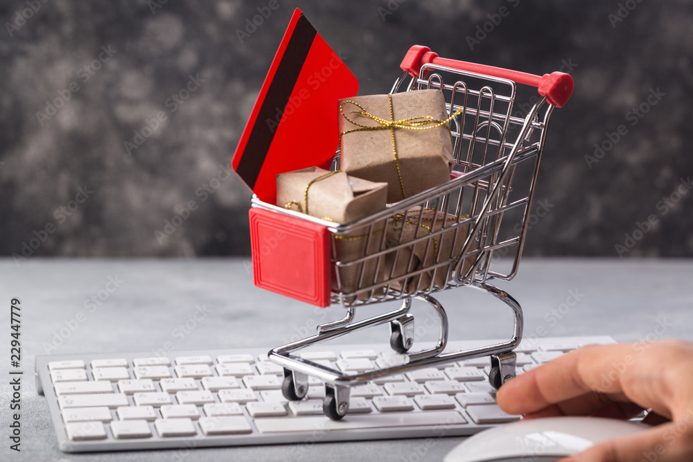 Christmas or New year gift paper box gold ribbon in a small shopping cart on a laptop keyboard. Concepts about online.e-commerce or electronic commerce is a transaction of buying or selling at home