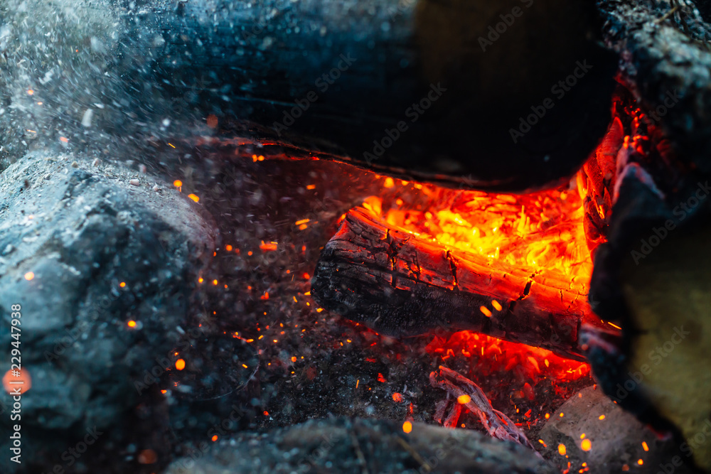 Smoldered logs burned in vivid fire close up. Atmospheric background with flame of campfire. Unimaginable detailed image of bonfire from inside with copy space. Whirlwind of smoke and glowing embers.
