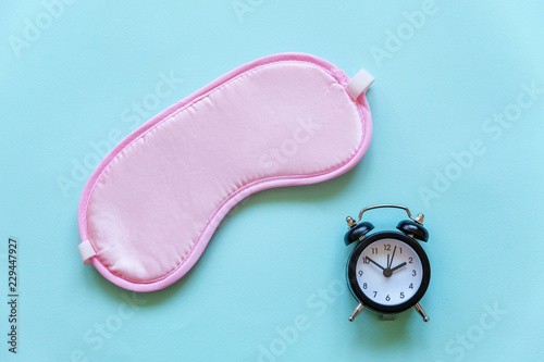 Sleeping eye mask, alarm clock isolated on blue pastel colourful trendy background. Do not disturb me, let me sleep. Rest, good night, siesta, insomnia, relaxation, tired, travel concept