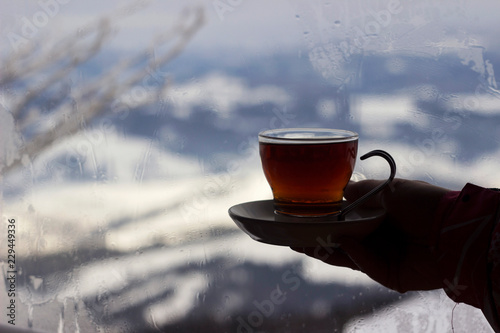 Girl holding a glass Cup of tea on the background of the window, outside the window the snow-capped mountains