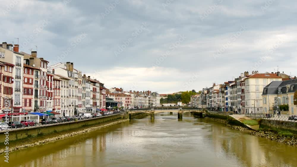 The Pannecau bridge is a Bayonne footbridge that crosses the Nive river. On either side of the shoreline, there are typical old houses. Filmed in a cloudy day. The Pannecau bridge is a Bayonne footbridge that crosses the Nive river. On either side of the shoreline, there are typical old houses. Filmed in a cloudy day.