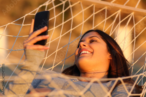 Happy girl resting on a hammock using a smart phone
