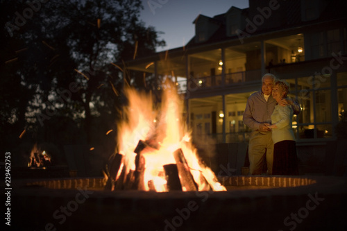 Happy senior couple standing close together next to an outdoor fire. photo