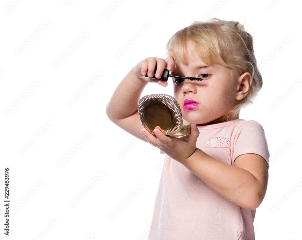 Fototapeta premium attractive young caucasian little girl doing makeup applying mascara looking in the mirrow studio shot isolated on white