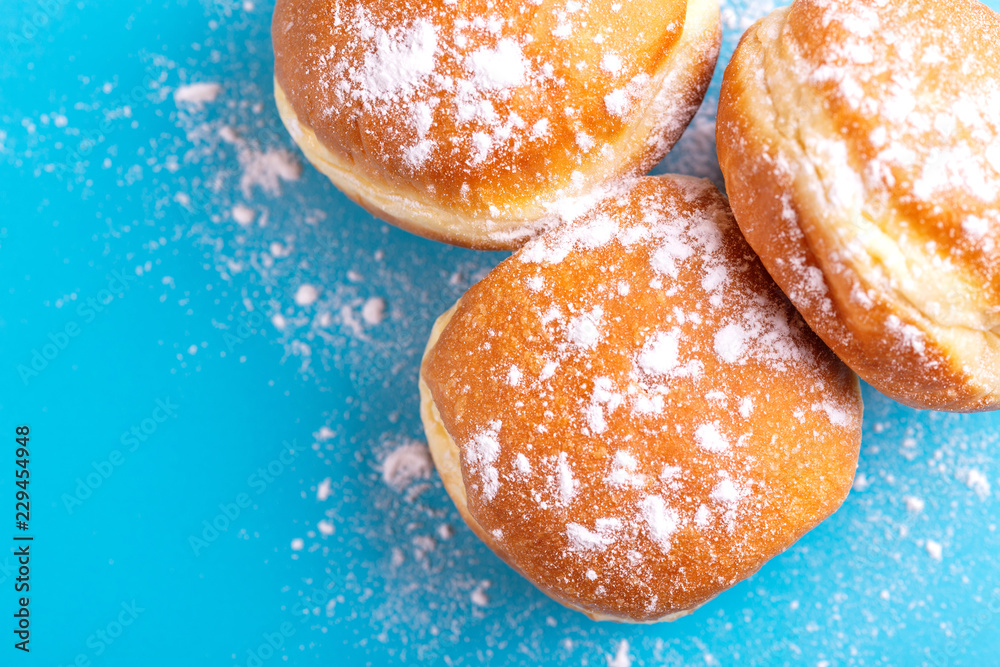Tasty sweet donuts with powdered sugar on bright blue background Tasty sweet donuts with powdered sugar on bright blue background