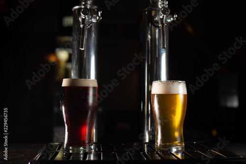 Two pint glasses of beer, a golden one and a dark one on the bar tab.
