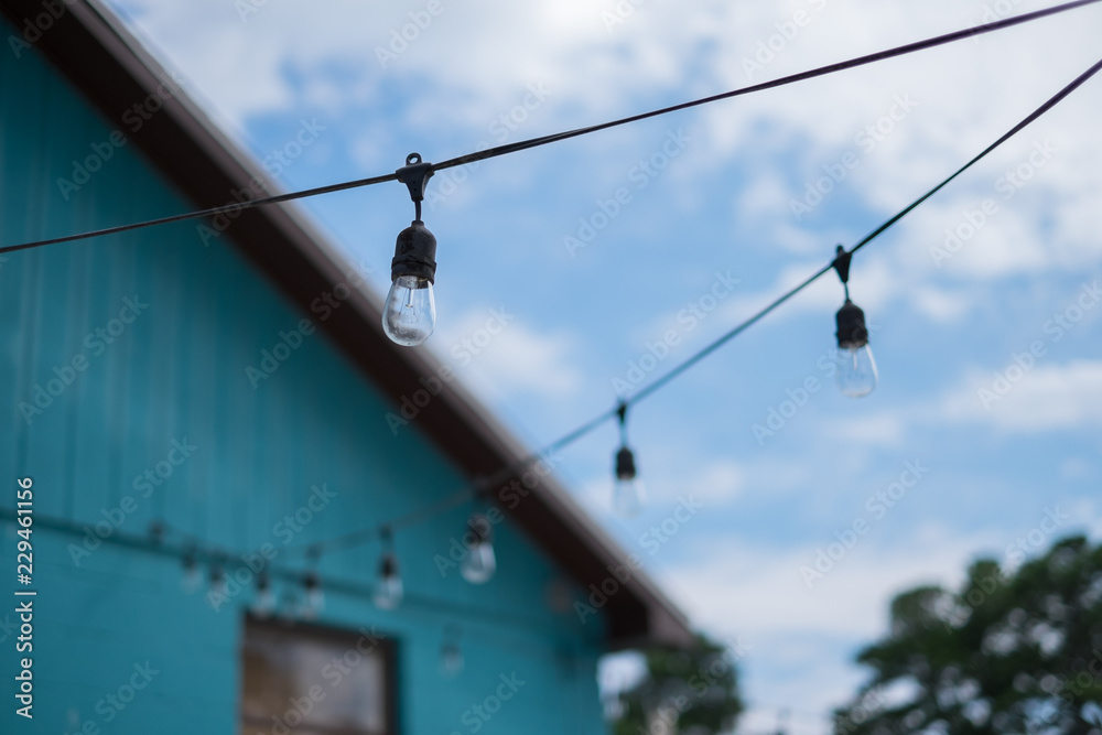 LIGHT BULBS ON STRING WIRE WITH BLUR GREEN HOUSE AND SKY BACKGROUND