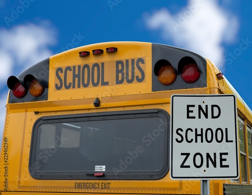 SIGN " END SCHOOL ZONE" WITH BACK OF A SCHOOL BUS AND BRIGHT BLUE SKY BACKGROUND