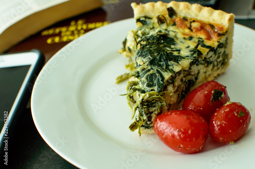 French cuisine healthy eating spinach quiche next to mobile phone and cookbook on plate ready to eat with fresh cherry tomatoes