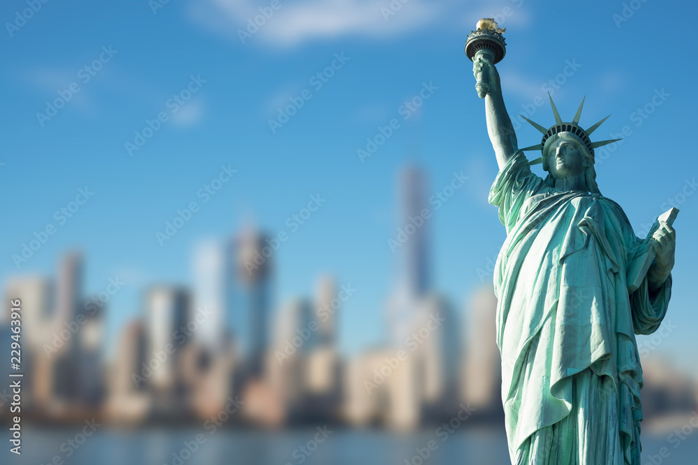 Fototapeta premium STATUE OF LIBERTY WITH BLUR BACKGROUND OF SKYSCRAPERS IN MANHATTAN, NEW YORK, USA