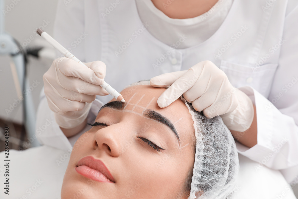 Young woman getting prepared for procedure of permanent eyebrow makeup in tattoo salon, closeup