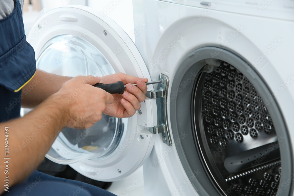 Young plumber fixing washing machine in bathroom, closeup Young plumber fixing washing machine in bathroom, closeup