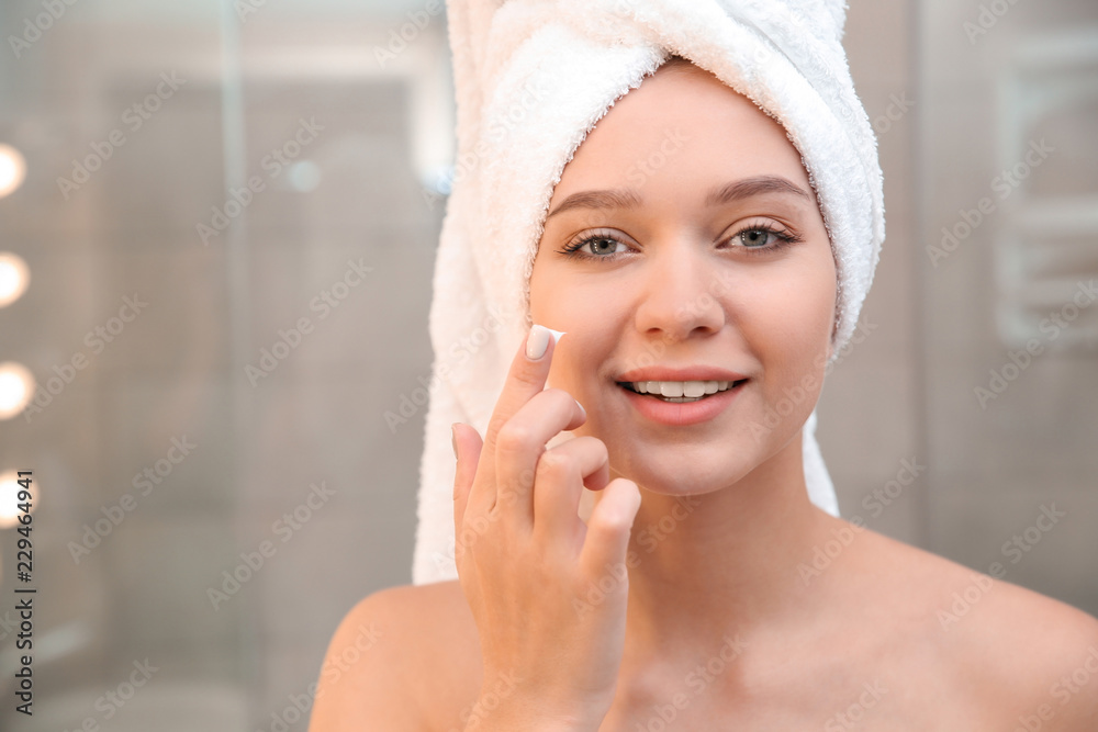 Beautiful woman with towel on head applying face cream in bathroom Beautiful woman with towel on head applying face cream in bathroom