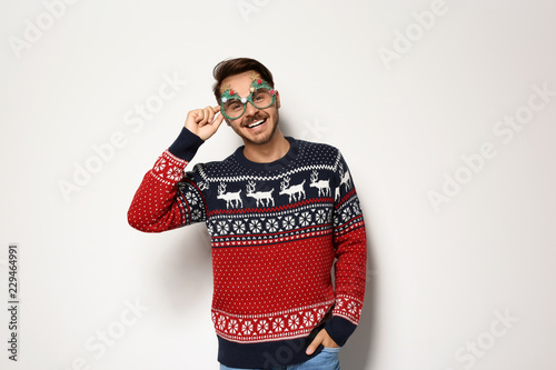 Young man in Christmas sweater with party glasses on white background